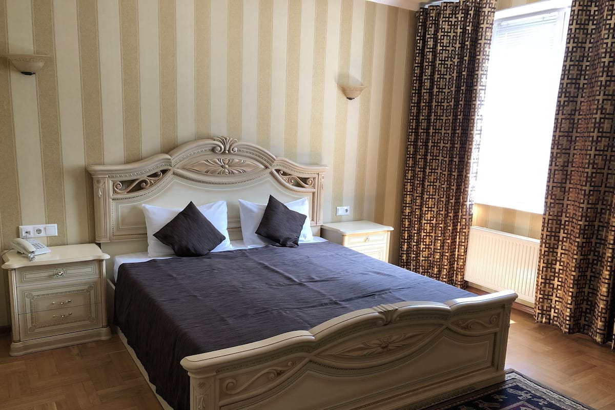 Une chambre à coucher bien rangée, avec un lit classique, des tables de chevet et un rideau à motifs.