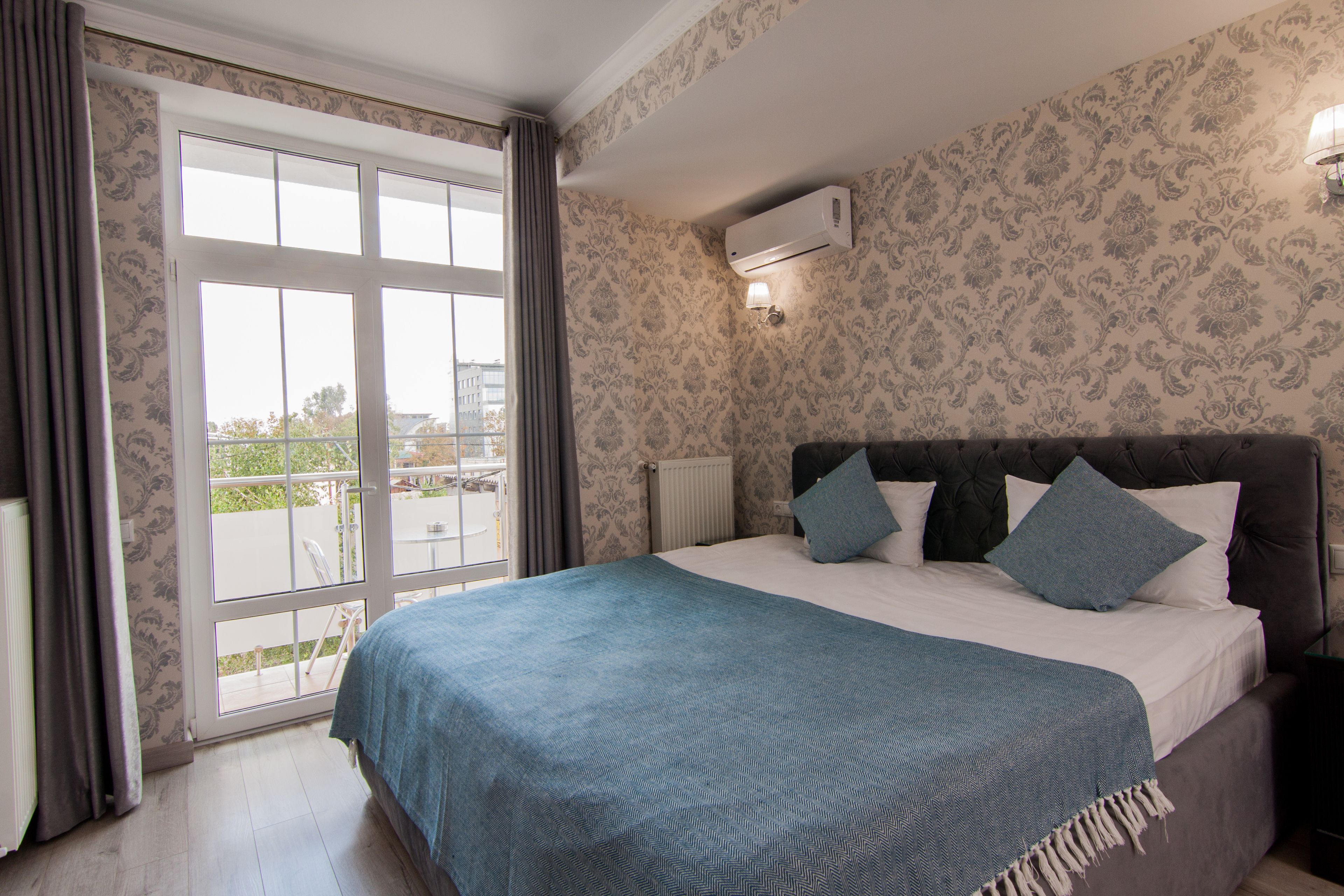 A bedroom with a large bed, a window with curtains, a radiator, and a wall-mounted air conditioner.