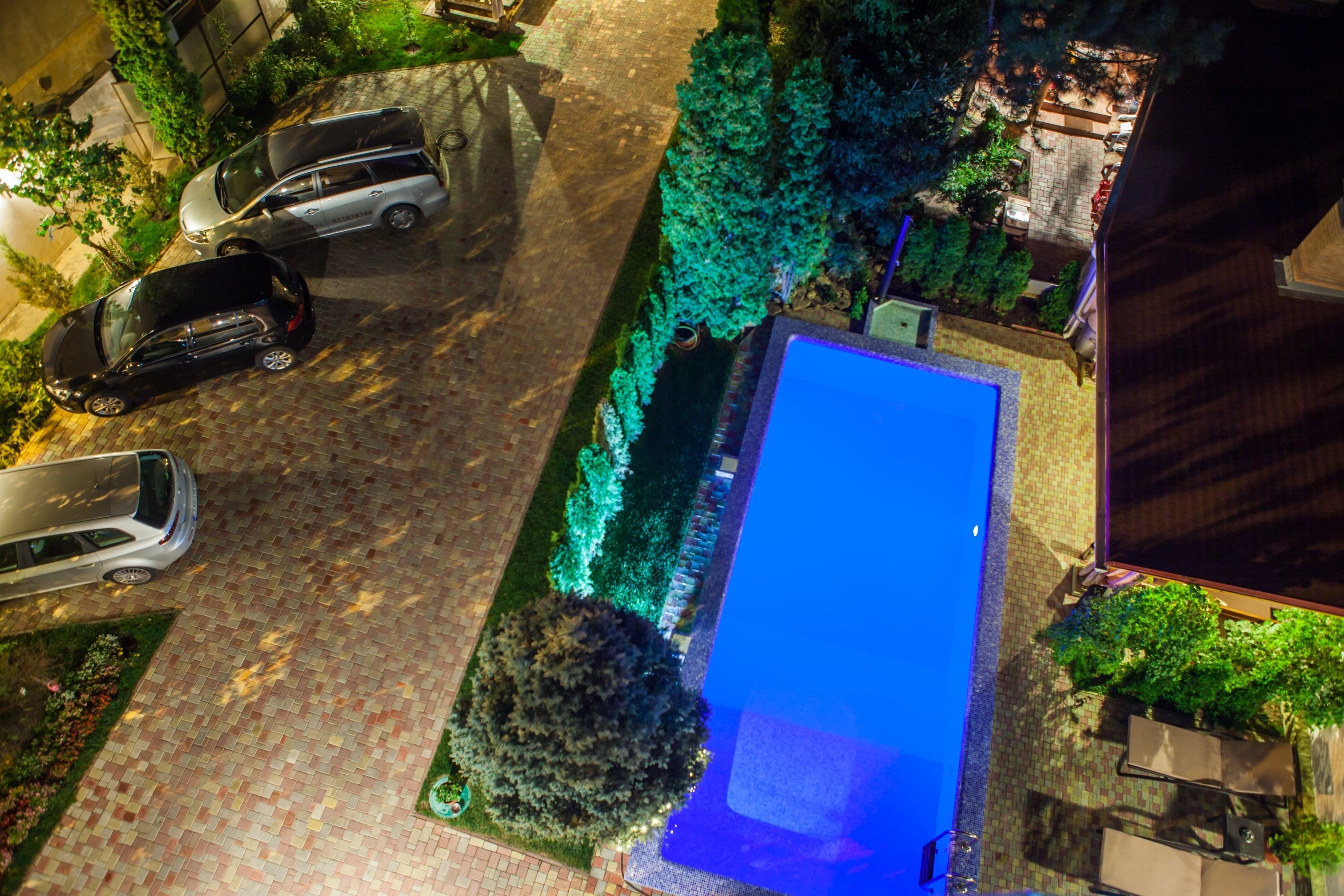Une vue aérienne d’une piscine entourée de verdure et bordée de voitures garées.