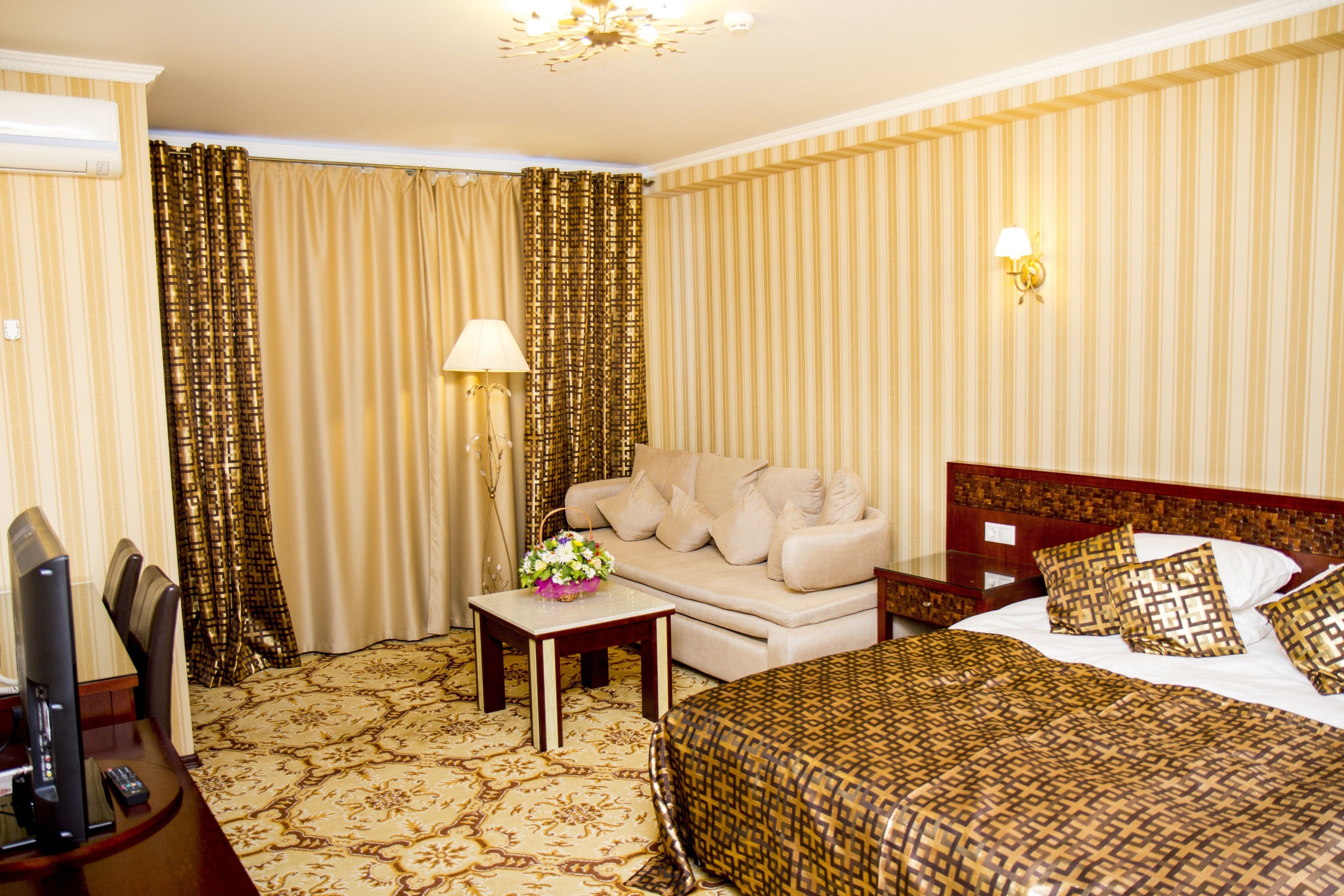 A hotel room with a bed, a sofa, a TV, and a lamp.