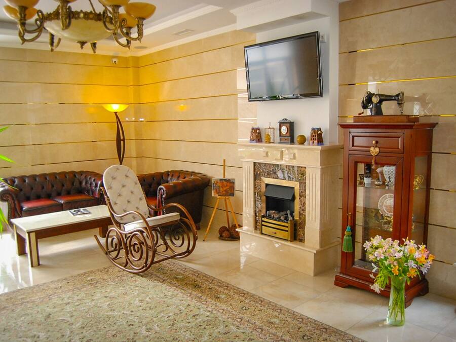Una sala de estar con chimenea, televisor montado en la pared, sofá, mecedora y un florero con flores.
