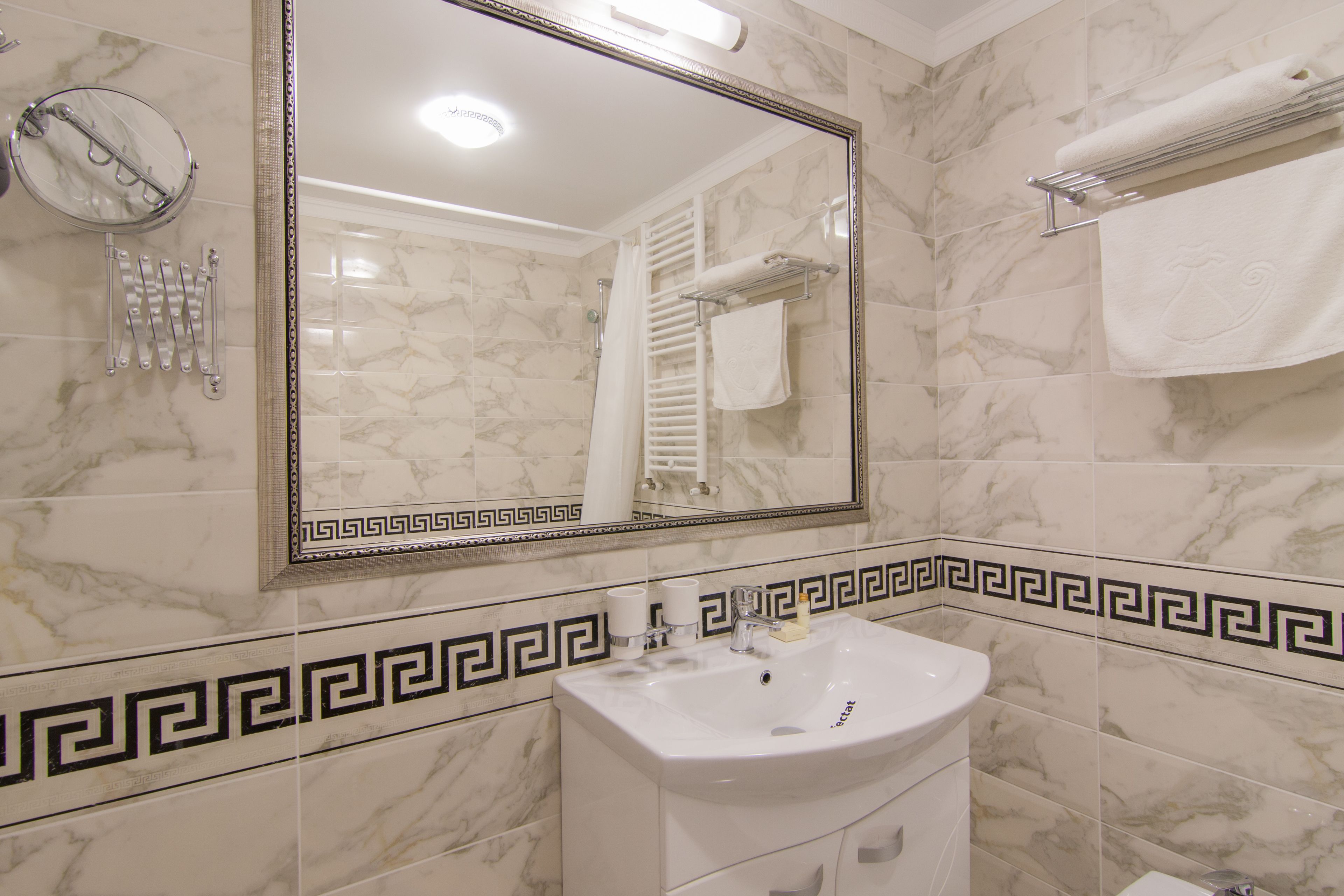 Une salle de bain avec un mur recouvert de carreaux de marbre, un lavabo blanc, un miroir et un porte-serviettes.