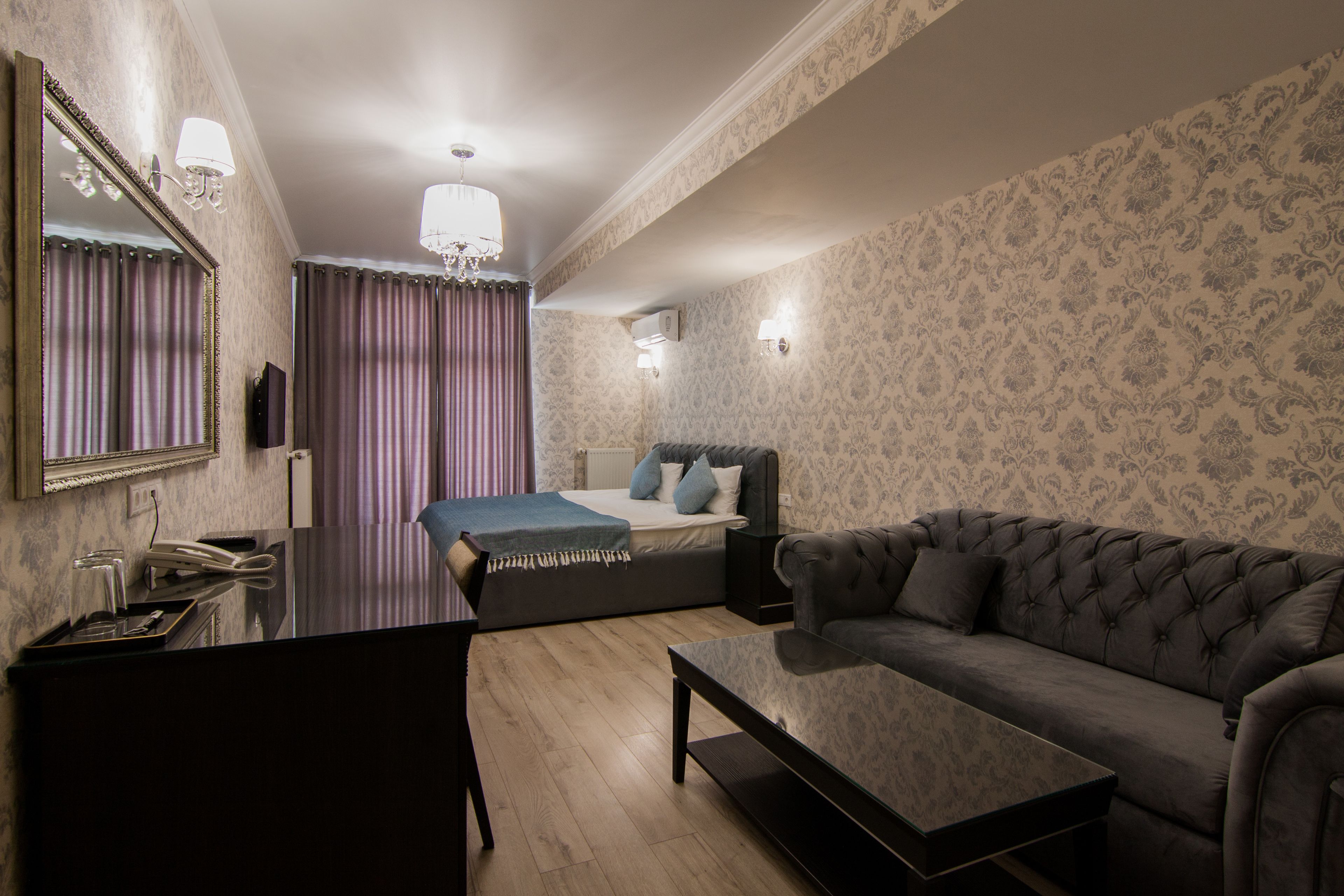 A hotel room with a bed, a sofa, a coffee table, a desk, and a mirror.