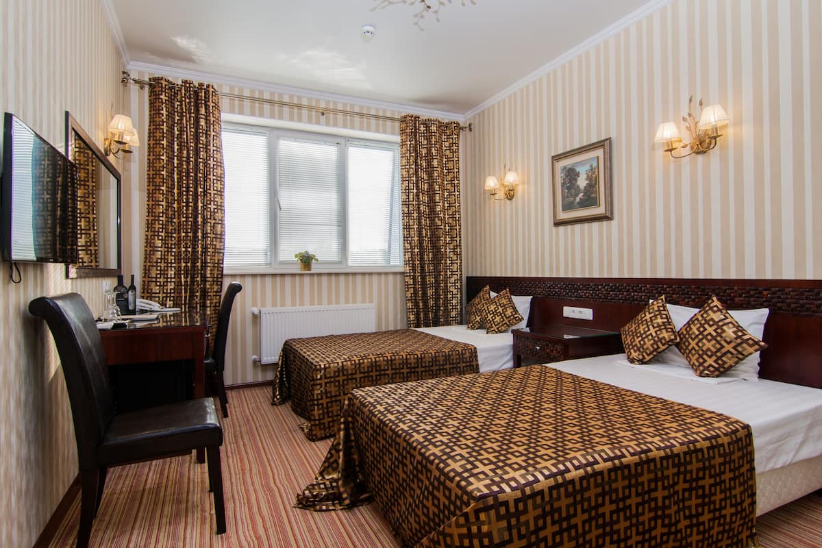 Une chambre d’hôtel avec deux lits, un bureau avec une chaise, une télévision et une fenêtre avec des rideaux.