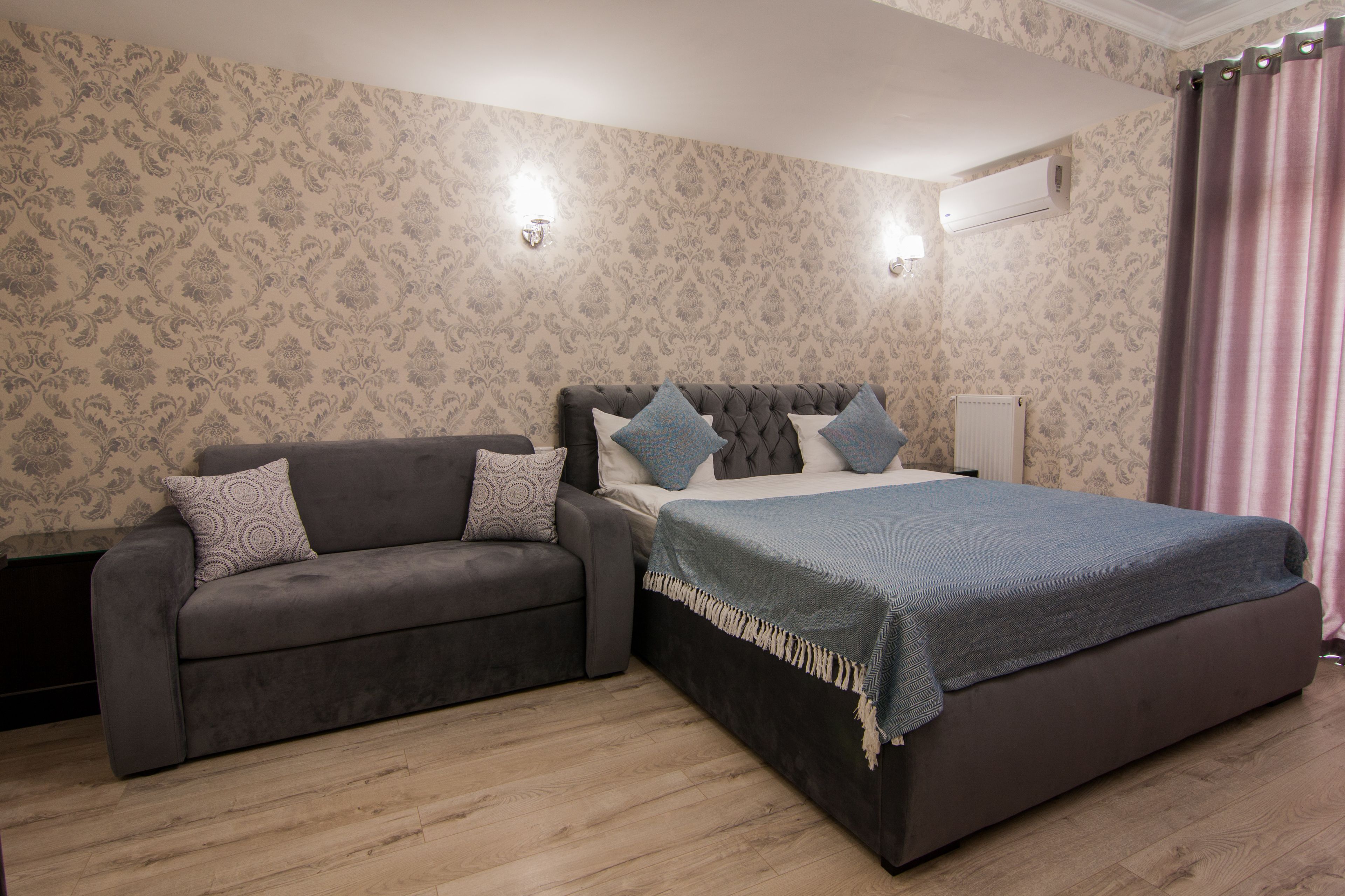 A bedroom with a bed, a sofa, and a wall-mounted air conditioner.