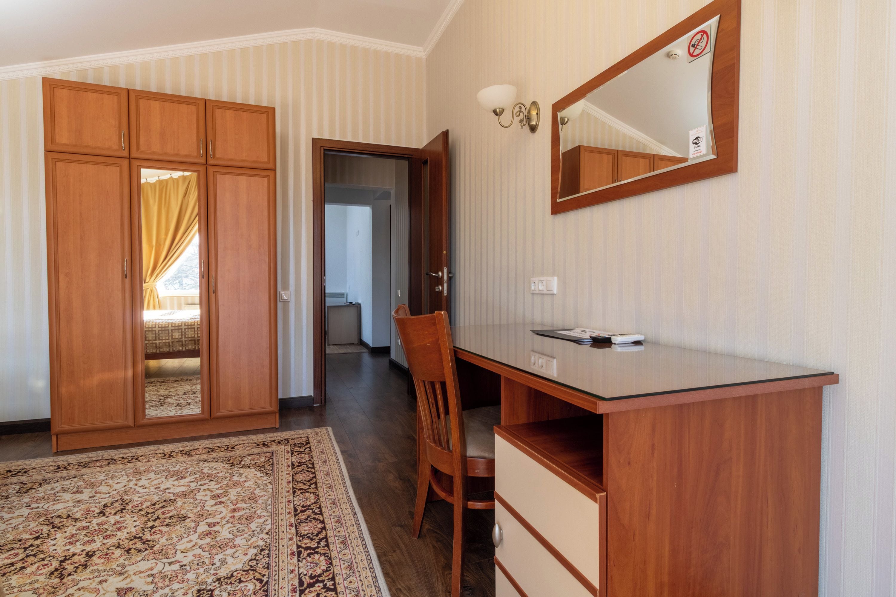 A hotel room with a wooden desk, a chair, a large mirror, and a wardrobe.