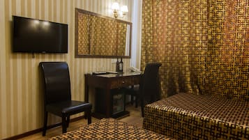 Una camera d'albergo con TV, una scrivania con sedia, un letto e tende a motivi.