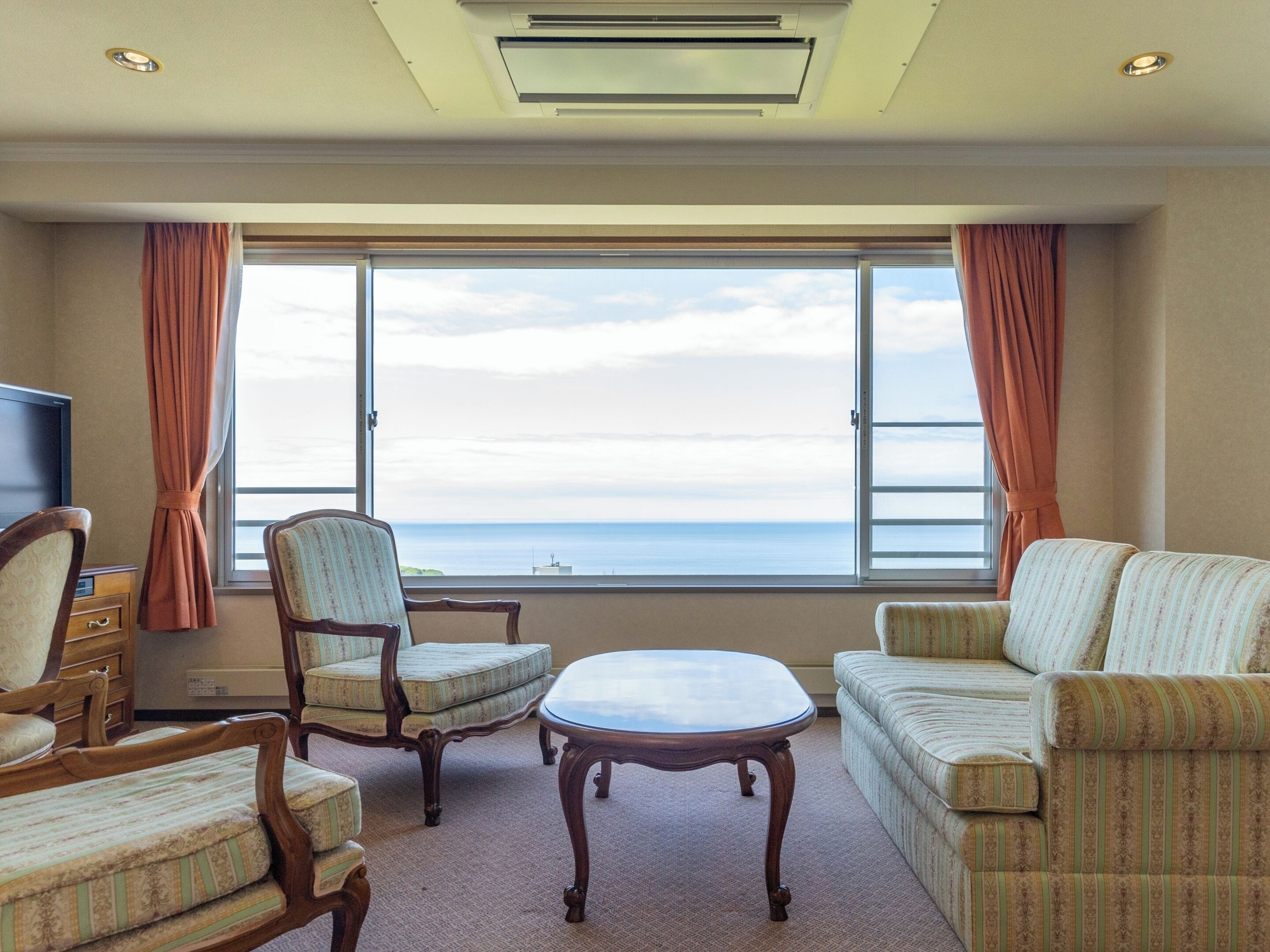 Une chambre d’hôtel dotée d’une grande fenêtre donnant sur la mer, d’un canapé, d’un fauteuil, d’une petite table et d’un téléviseur.