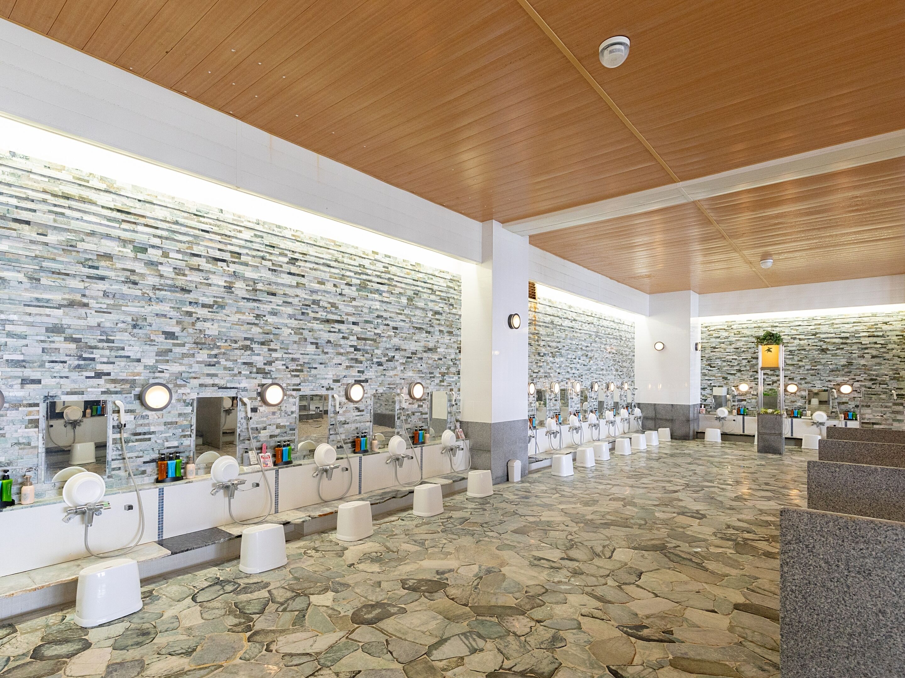 A modern restroom with stone tile floors, wooden ceiling, and multiple sinks with mirrors.