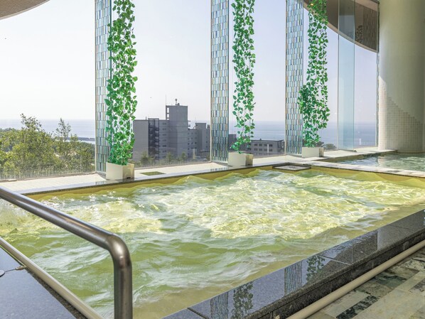 Un jacuzzi con vista a la ciudad, rodeado de paredes de vidrio y follaje.