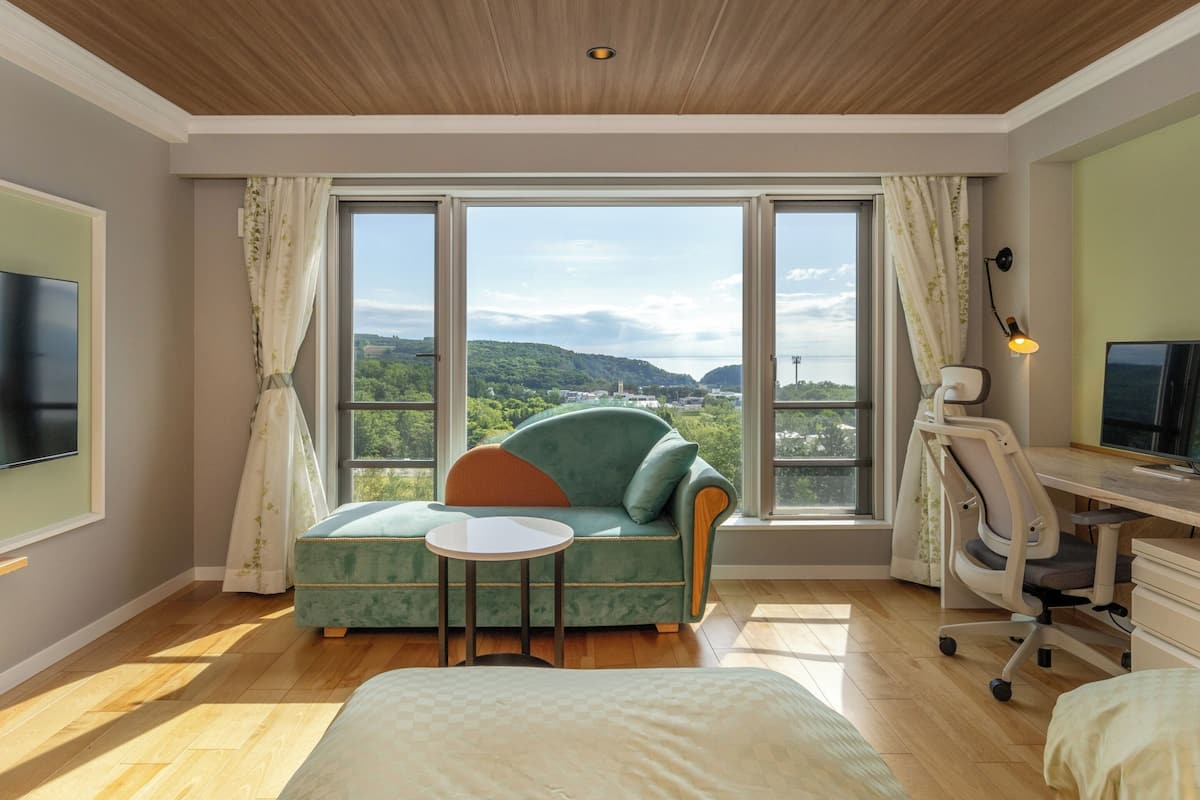 Un dormitorio moderno con un ventanal grande, un sofá verde, una mesita redonda pequeña, una cama y un escritorio con silla.