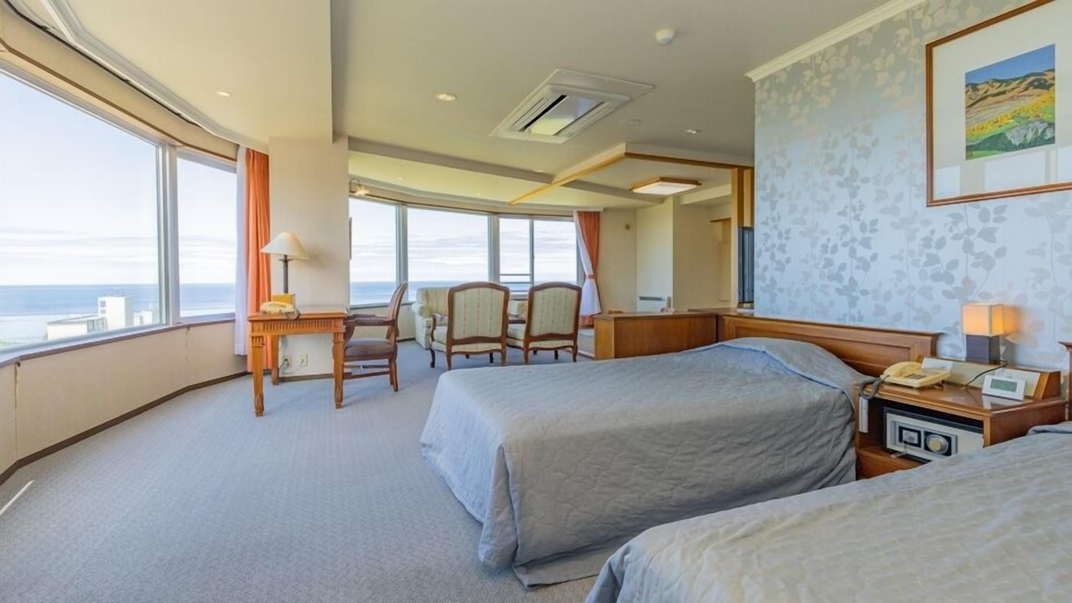 A hotel room with two beds, a desk with a telephone, a chair, and a large window offering a view.