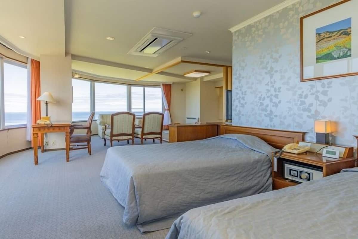 Habitación de hotel con dos camas, un escritorio con teléfono, una silla y un ventanal con vistas.