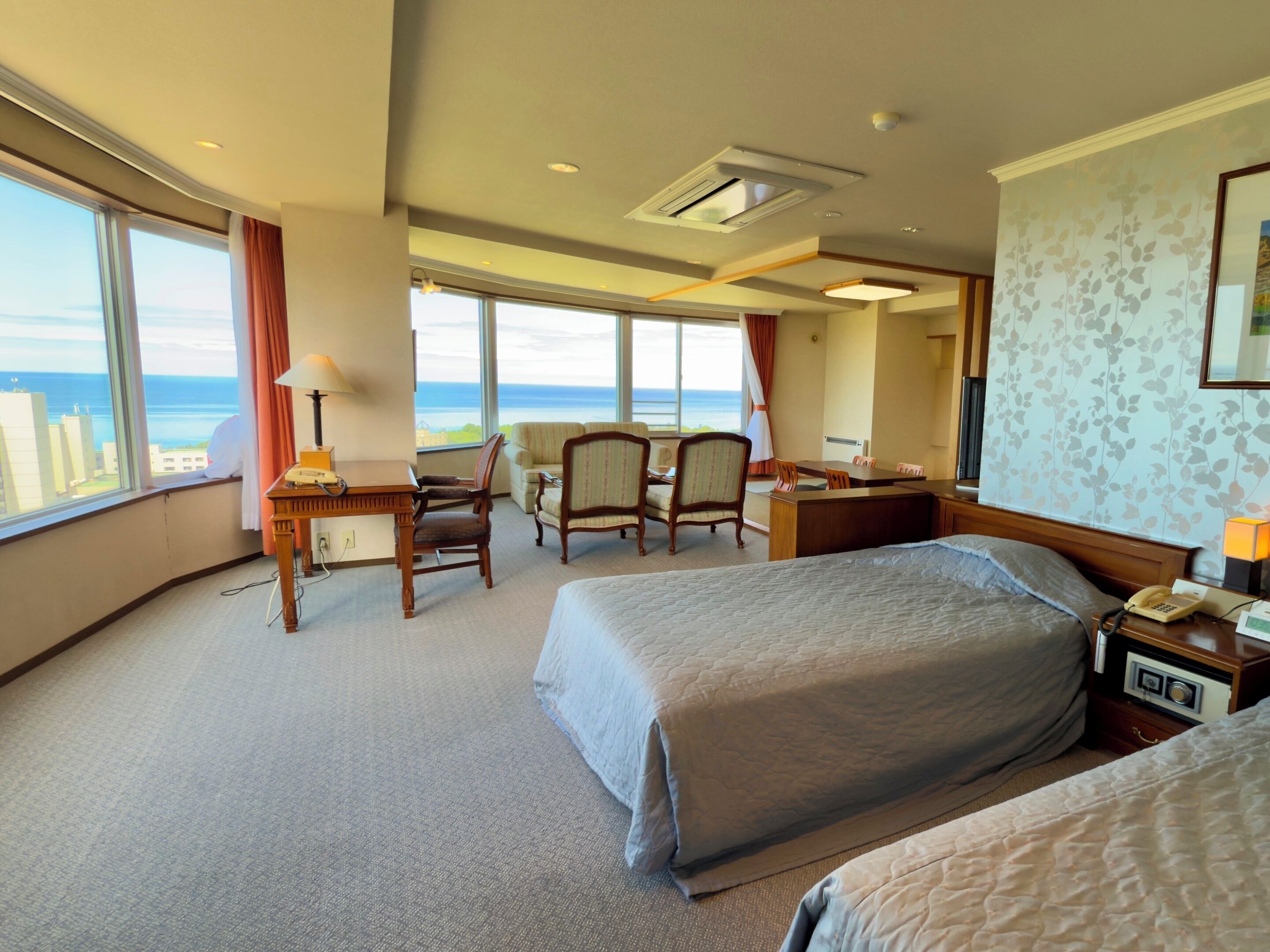 A hotel room with a large bed, a desk, a chair, and a view of the ocean.