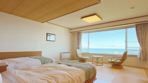 Ein Hotelzimmer mit einem großen Bett, zwei Stühlen, einem kleinen Tisch und Meerblick.