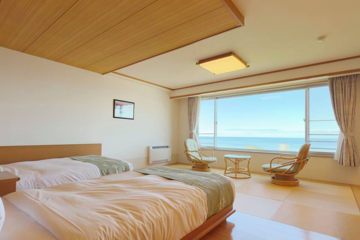 Habitación de hotel con una cama grande, dos sillas, una mesita y vista al mar.