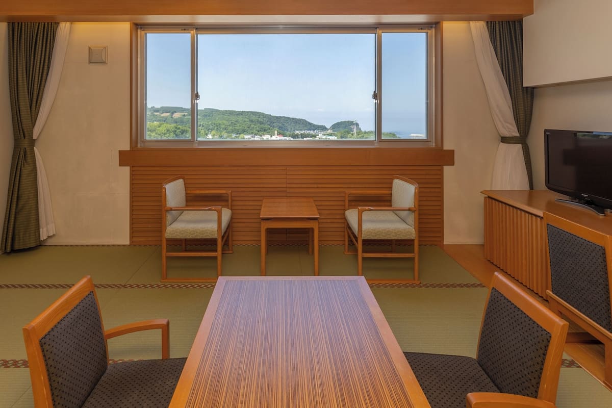 Una habitación con un ventanal grande, dos sillas, una mesa y un televisor.