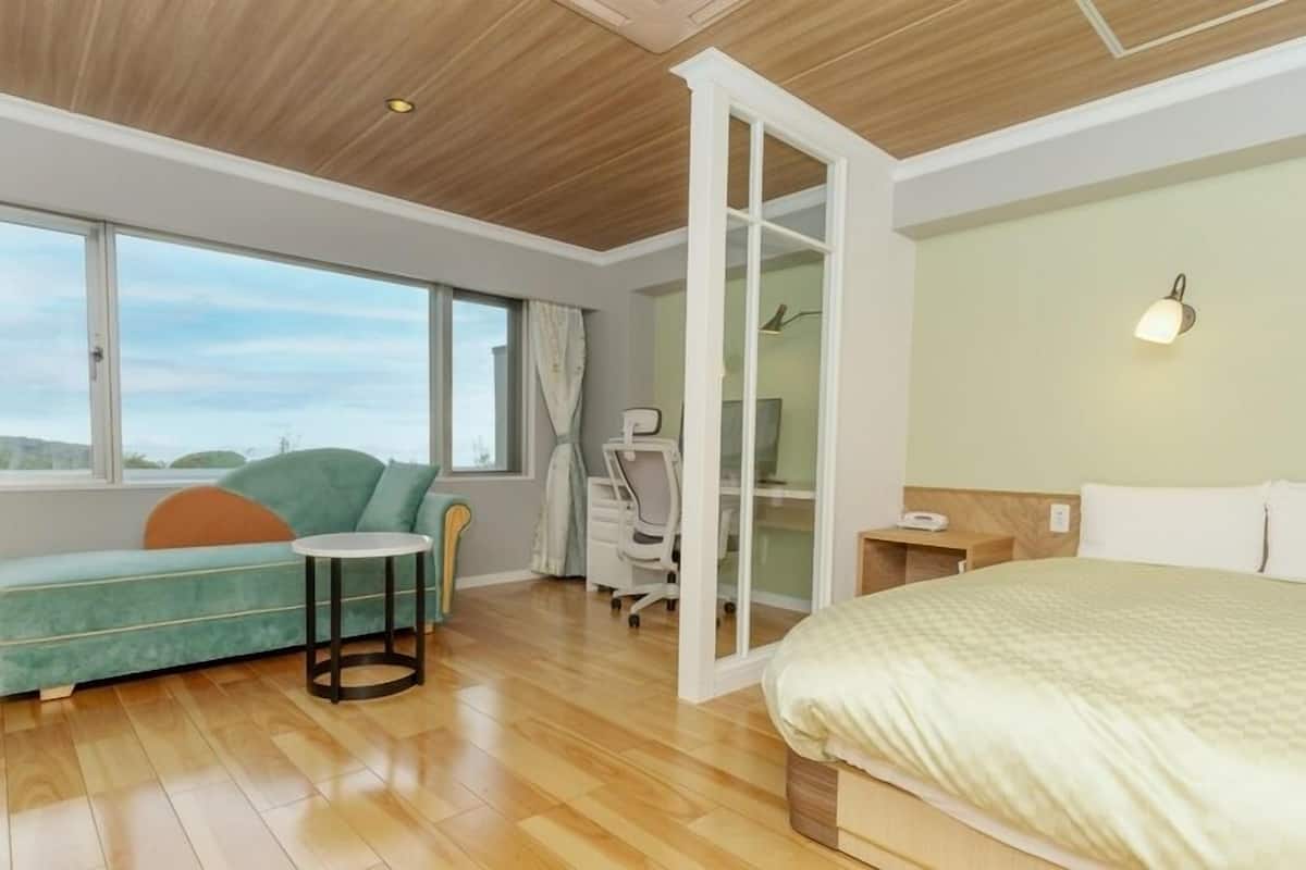 A bedroom with a bed, a desk, a chair, a small table, and a sofa.