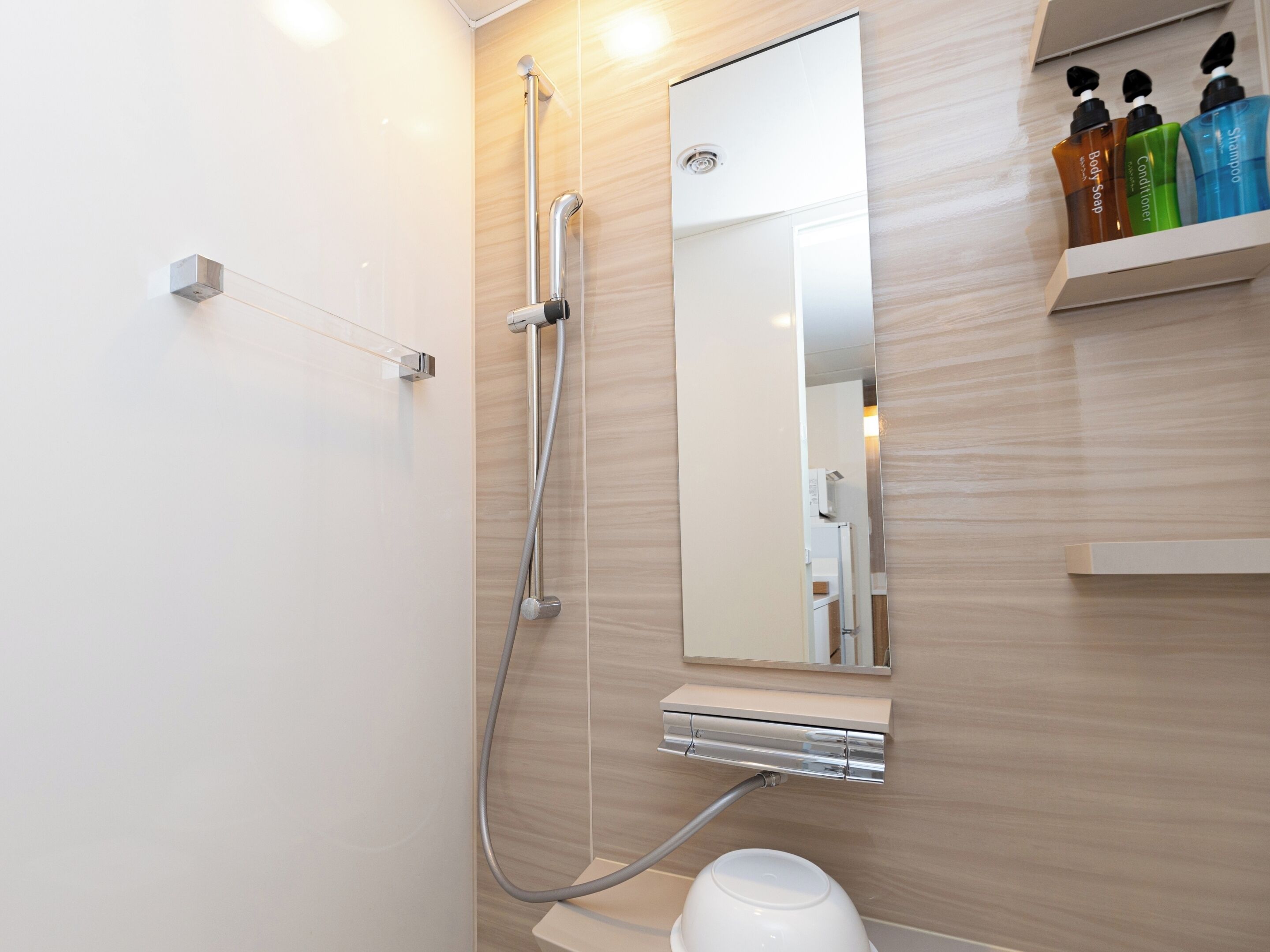 A modern bathroom with a shower, a mirror, and a shelf with toiletries.