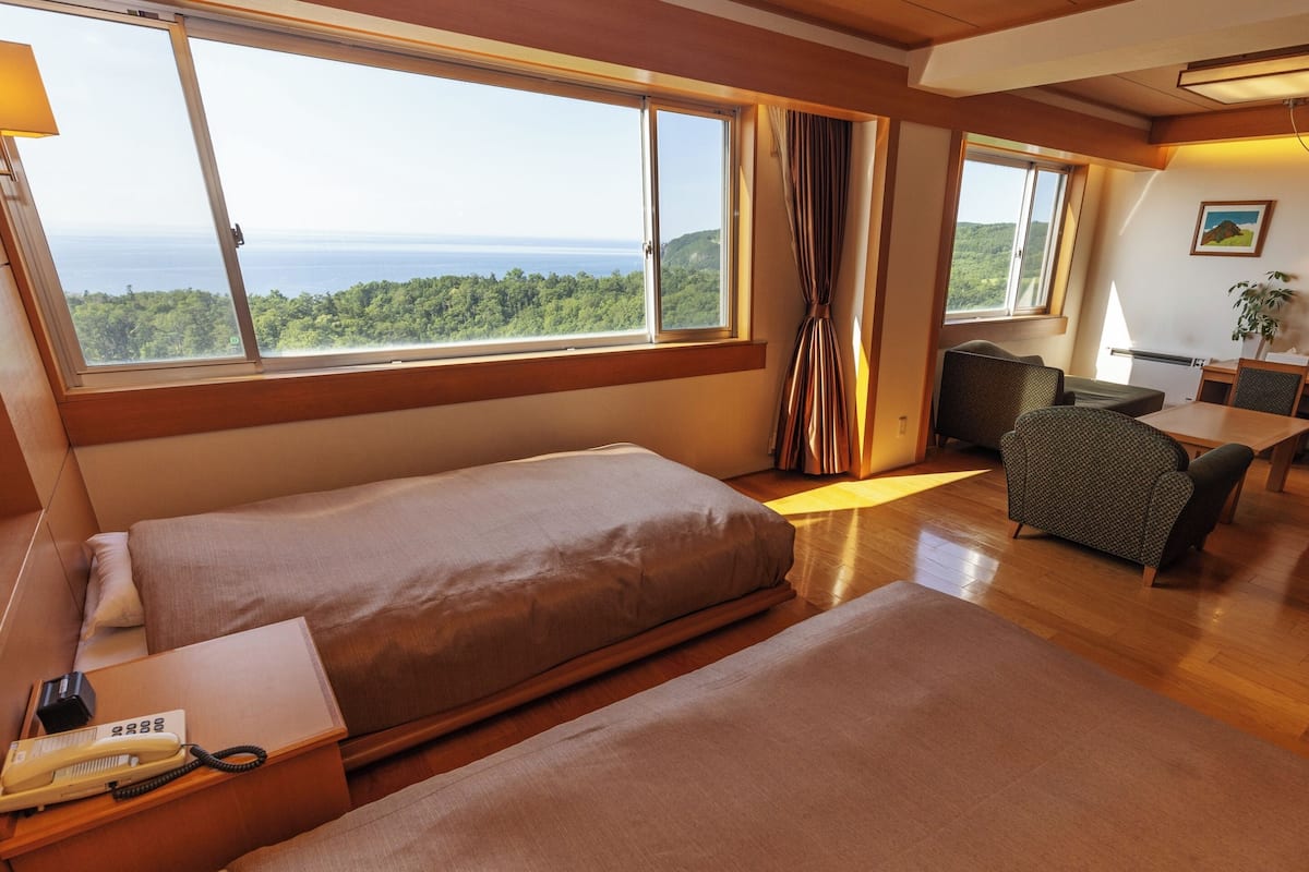 Habitación de hotel con dos camas, un escritorio, una silla y vistas al mar.