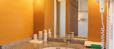 Un baño con encimera de granito, un lavabo, un espejo y un secador de pelo sobre un soporte.