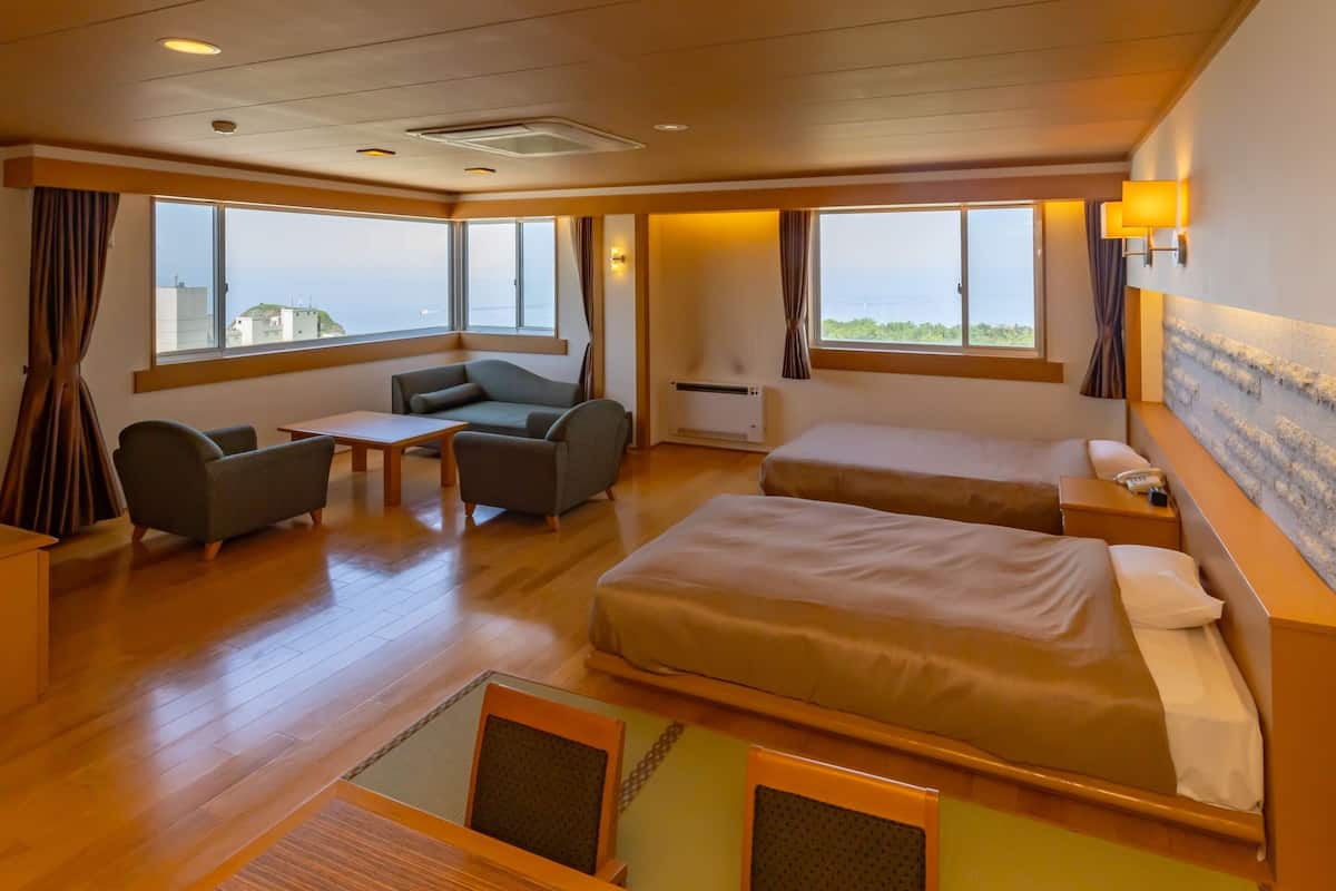 Habitación de hotel con sofá, dos camas individuales, una mesita y vista al mar.
