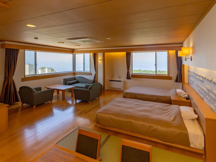 Ett hotellrum med en soffa, två enkelsängar, ett litet bord och utsikt över havet.