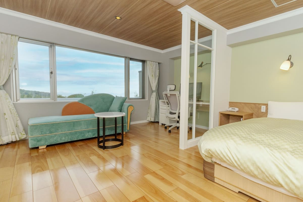 Una habitación de hotel moderna con techo de madera, una cama grande, un escritorio con computadora, una silla y un sofá.
