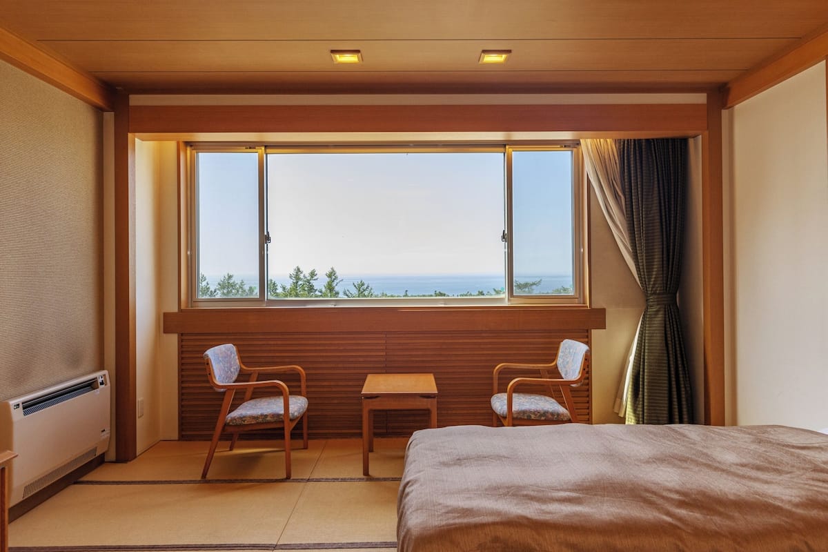 Habitación de hotel con un ventanal grande, dos sillas, una mesita y una cama.