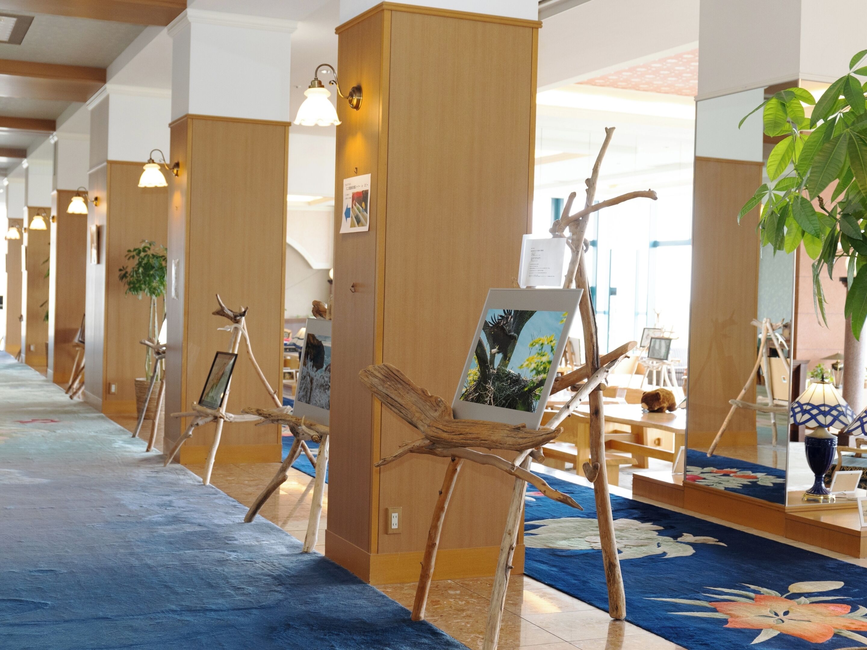A corridor with wooden pillars, artwork on branches, and a blue carpet.