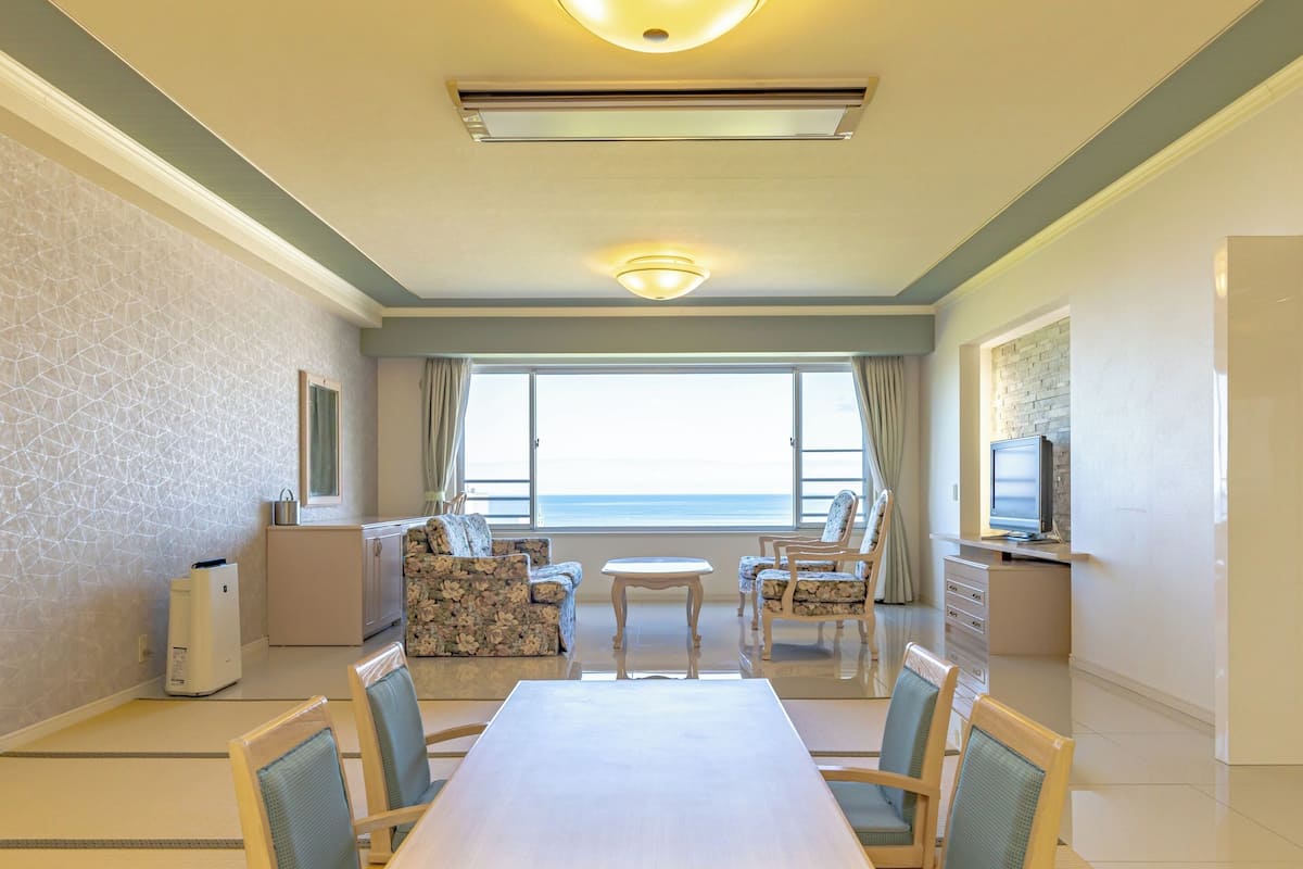 Habitación de hotel con una mesa de comedor, sillas, un sofá, un televisor y vista al mar.