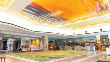 A spacious lobby with a colorful ceiling mural, a seating area with armchairs, and a reception desk.