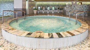 Ein Whirlpool mit Steinboden-Mosaik, Holzboden und einer Steinwand mit einem Fenster.