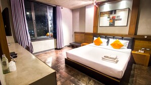 Una habitación de hotel con cama, mesita de noche, escritorio y ventana con cortinas.