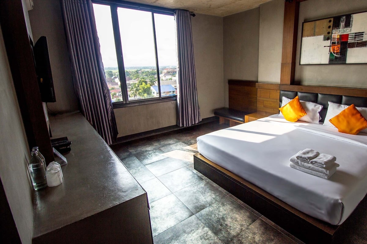 Une chambre d’hôtel avec un grand lit, un bureau, une chaise, une fenêtre avec des rideaux et un tableau au mur.