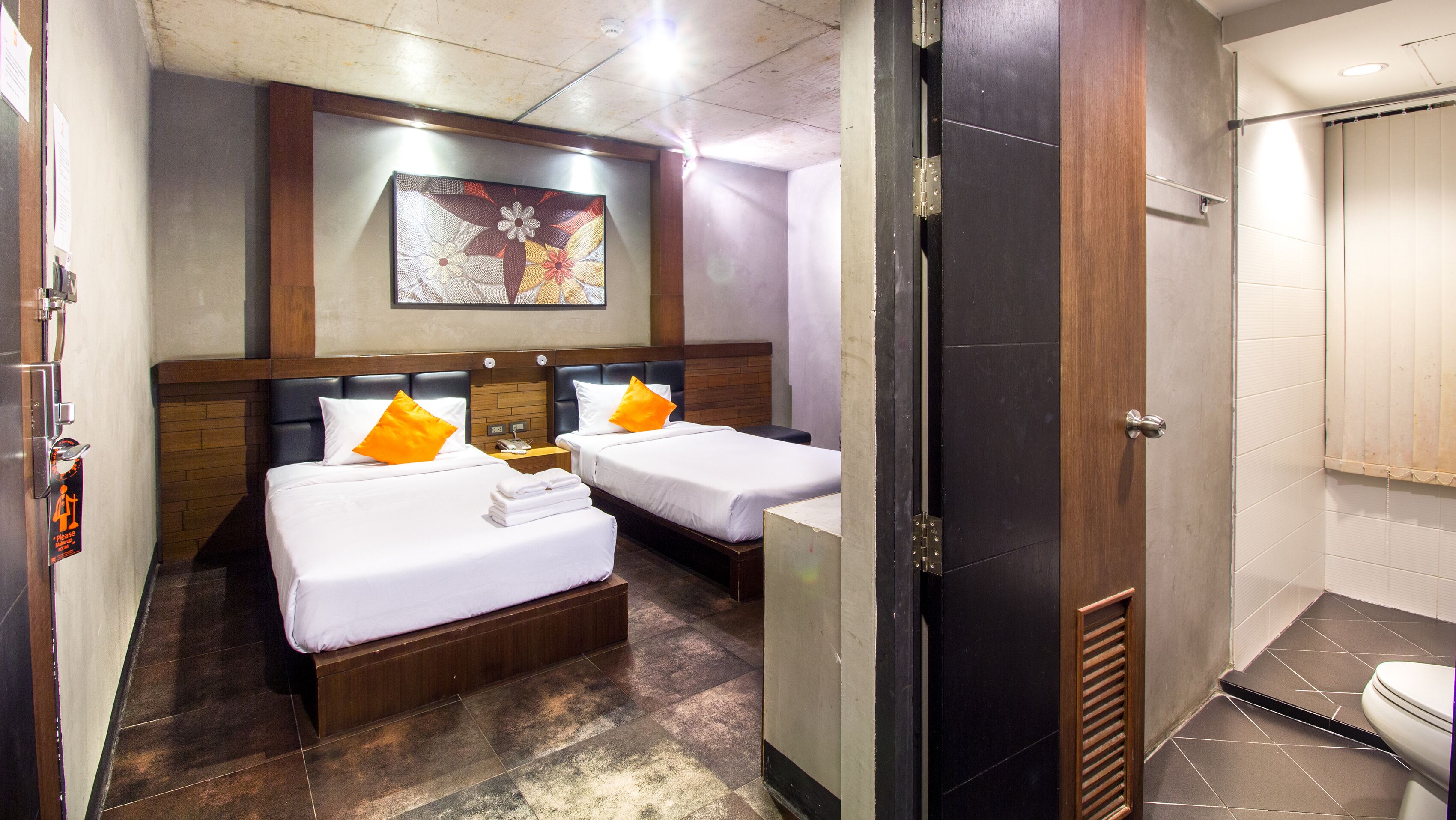 A hotel room with two beds, a wooden headboard, a painting on the wall, and a bathroom with a toilet and shower.