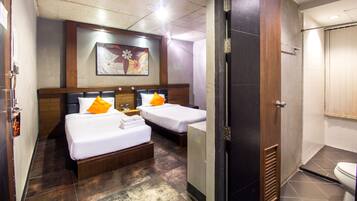 Une chambre d’hôtel avec deux lits, une tête de lit en bois, un tableau au mur et une salle de bain avec des toilettes et une douche.