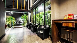 Un vestíbulo de hotel con zona de estar, mostrador de recepción y vistas a zonas verdes exteriores.