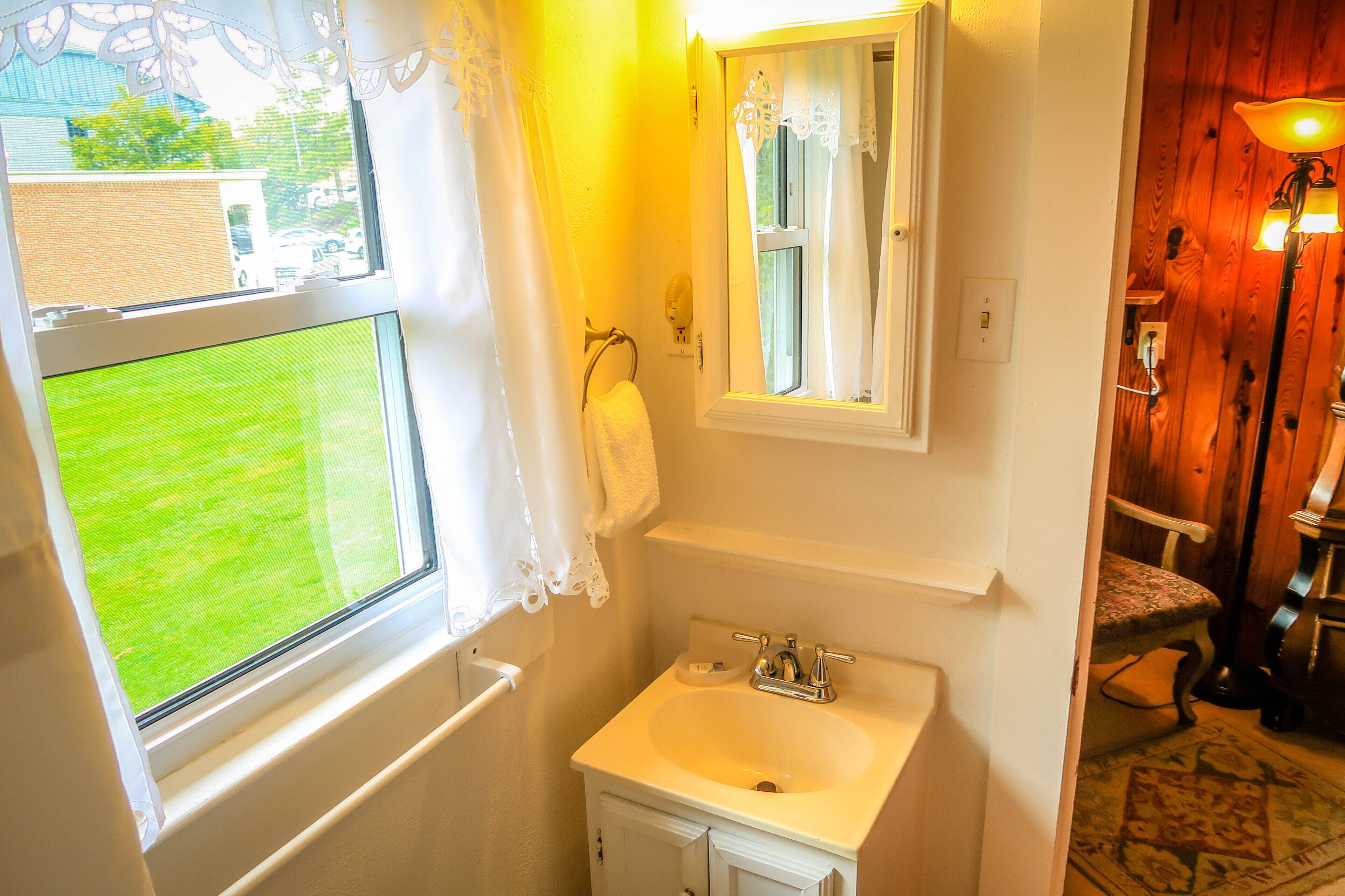A bathroom with a window, a sink, a mirror, and a chair.