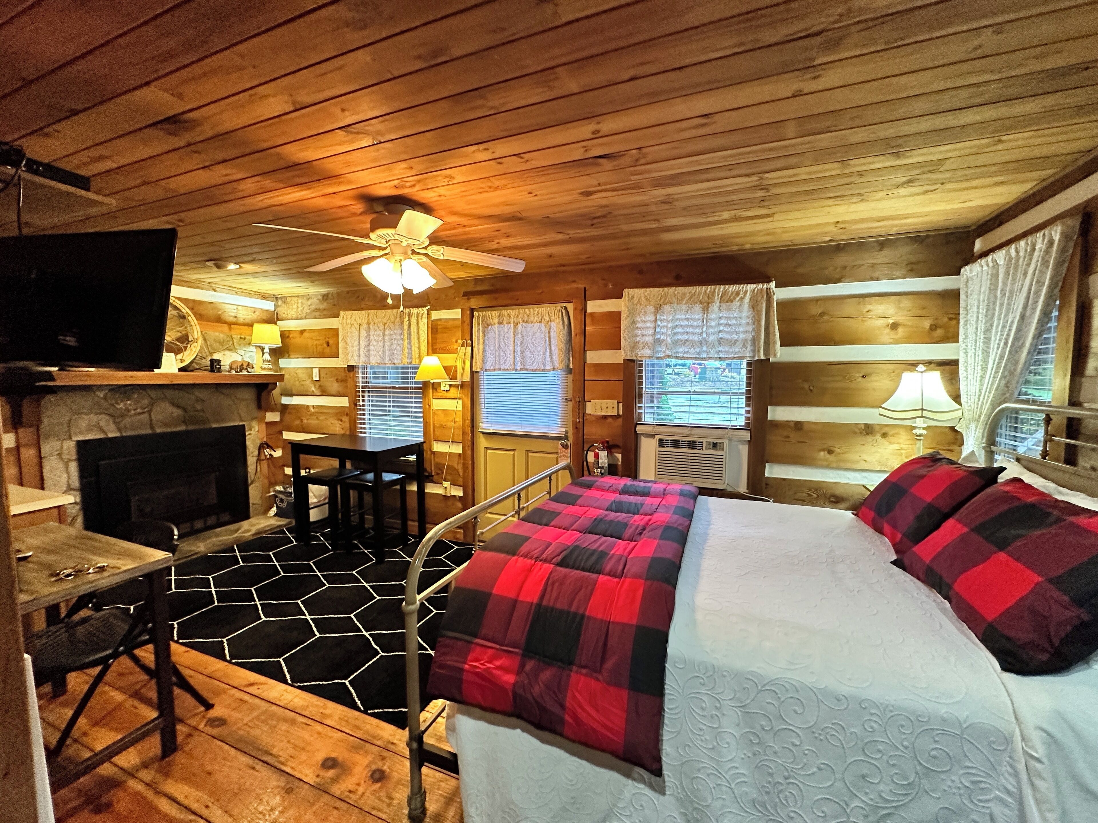 A cozy cabin room with a bed, a fireplace, a desk, and a ceiling fan.