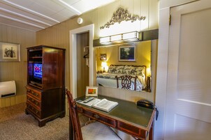 Una habitación de hotel con un aparador de madera, un escritorio con lámpara, una cama con cabecera y un televisor montado en la pared.