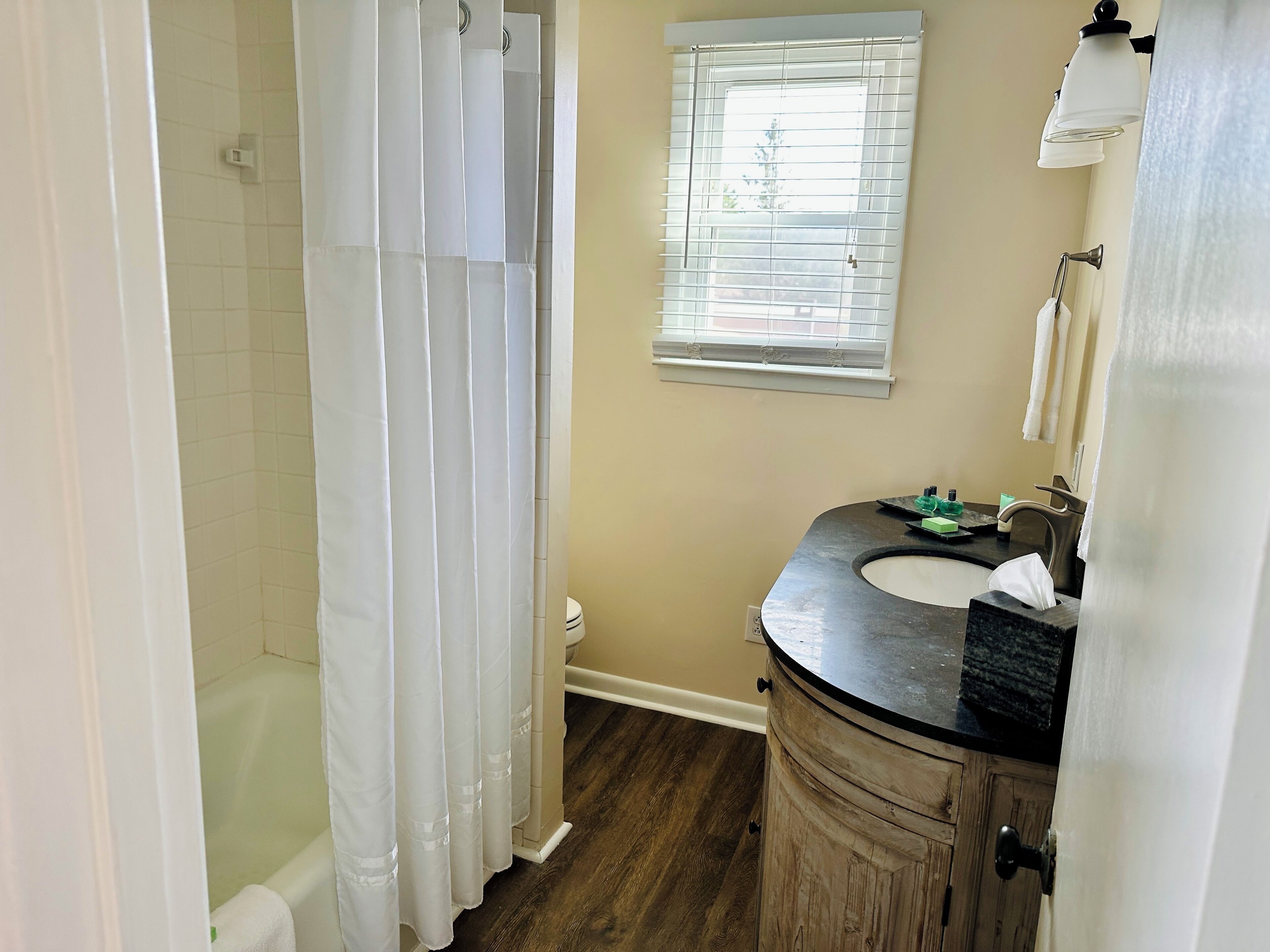 A bathroom with a bathtub, a sink, and a window with blinds.