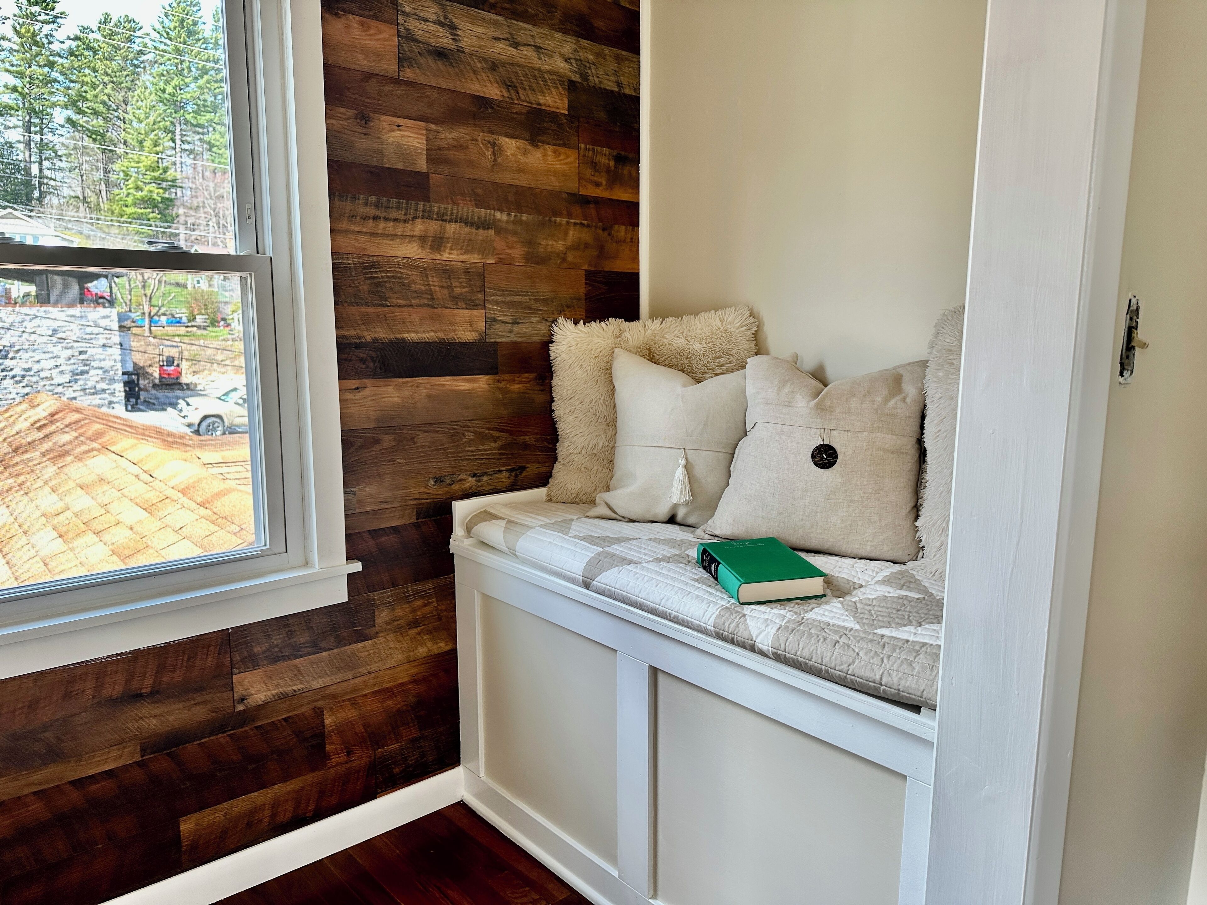 A corner room with a built-in bench, a window, and a view of the outside.