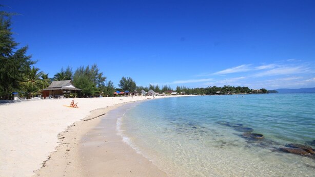 A beach with clear water, a sandy shore, and a few buildings in the background. - Phangan Cove (Ko Pha-ngan)