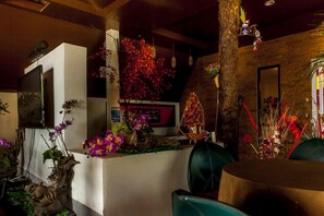 A room with a wooden ceiling, a stone wall, and a large window. There is a table with chairs and a plant on the windowsill.