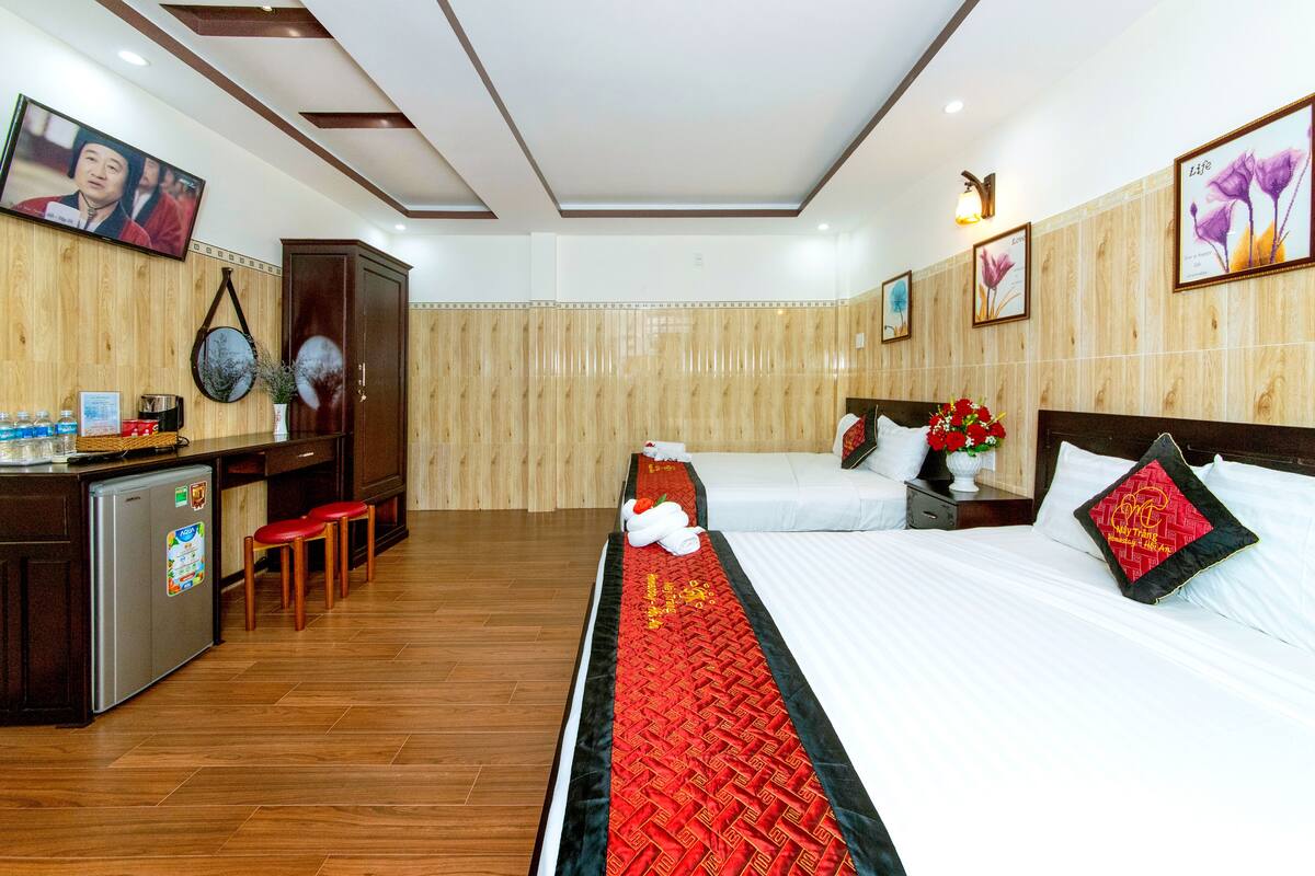 Habitación de hotel con dos camas, un escritorio con refrigerador y una televisión montada en la pared.