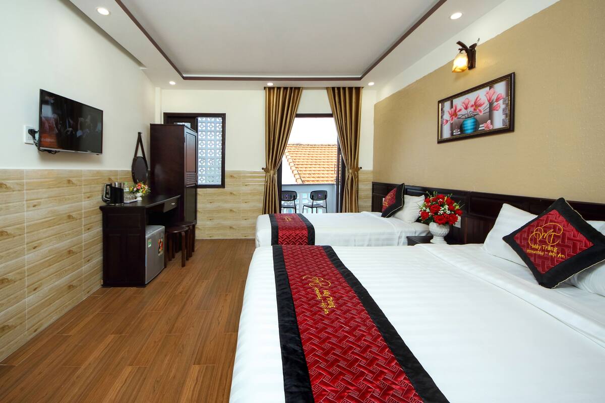 Habitación de hotel con dos camas, televisión, escritorio y ventana con cortinas.