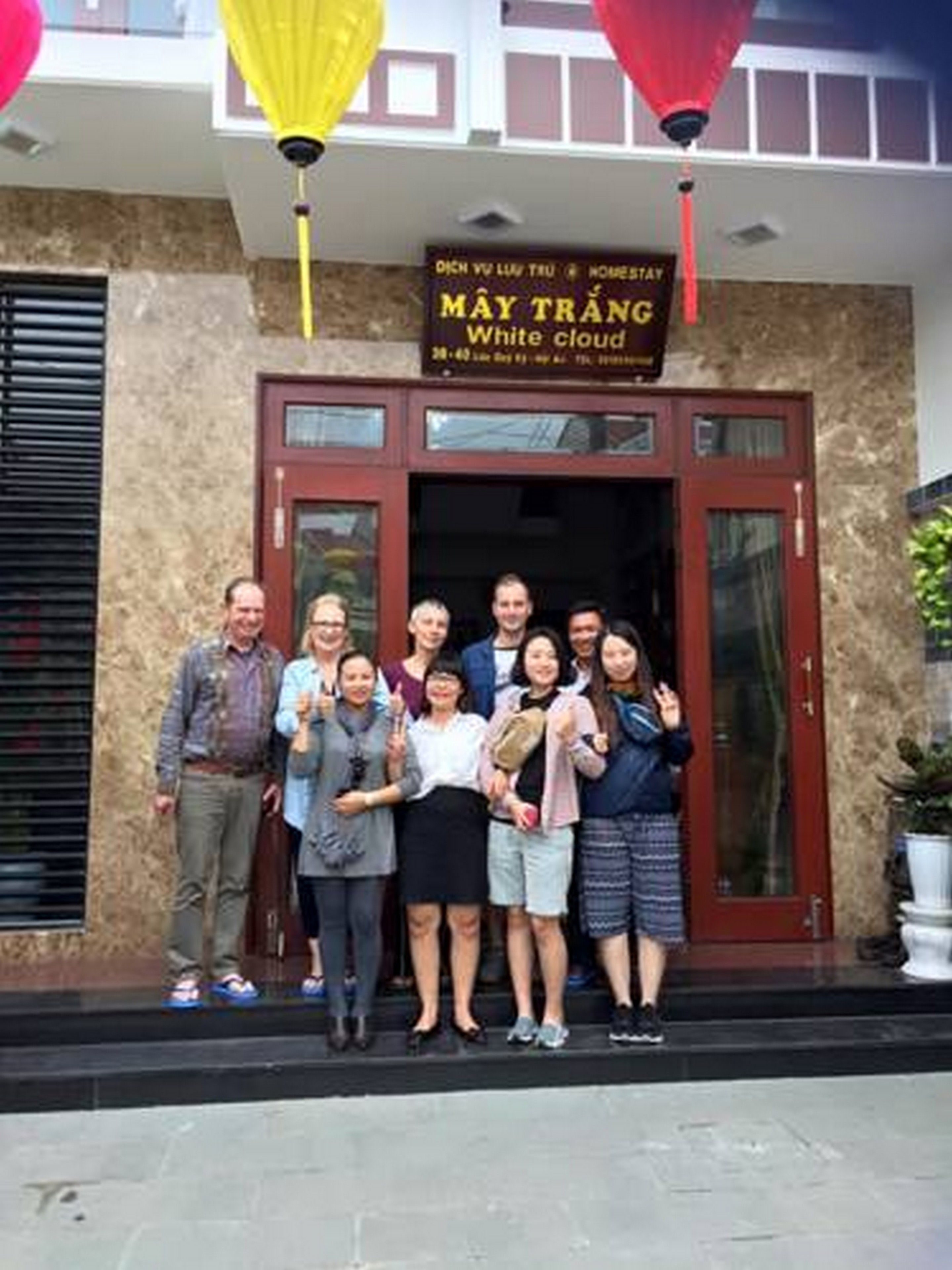 Un grupo de personas de pie frente a un edificio con un letrero que dice "MAY TRANG White Cloud".