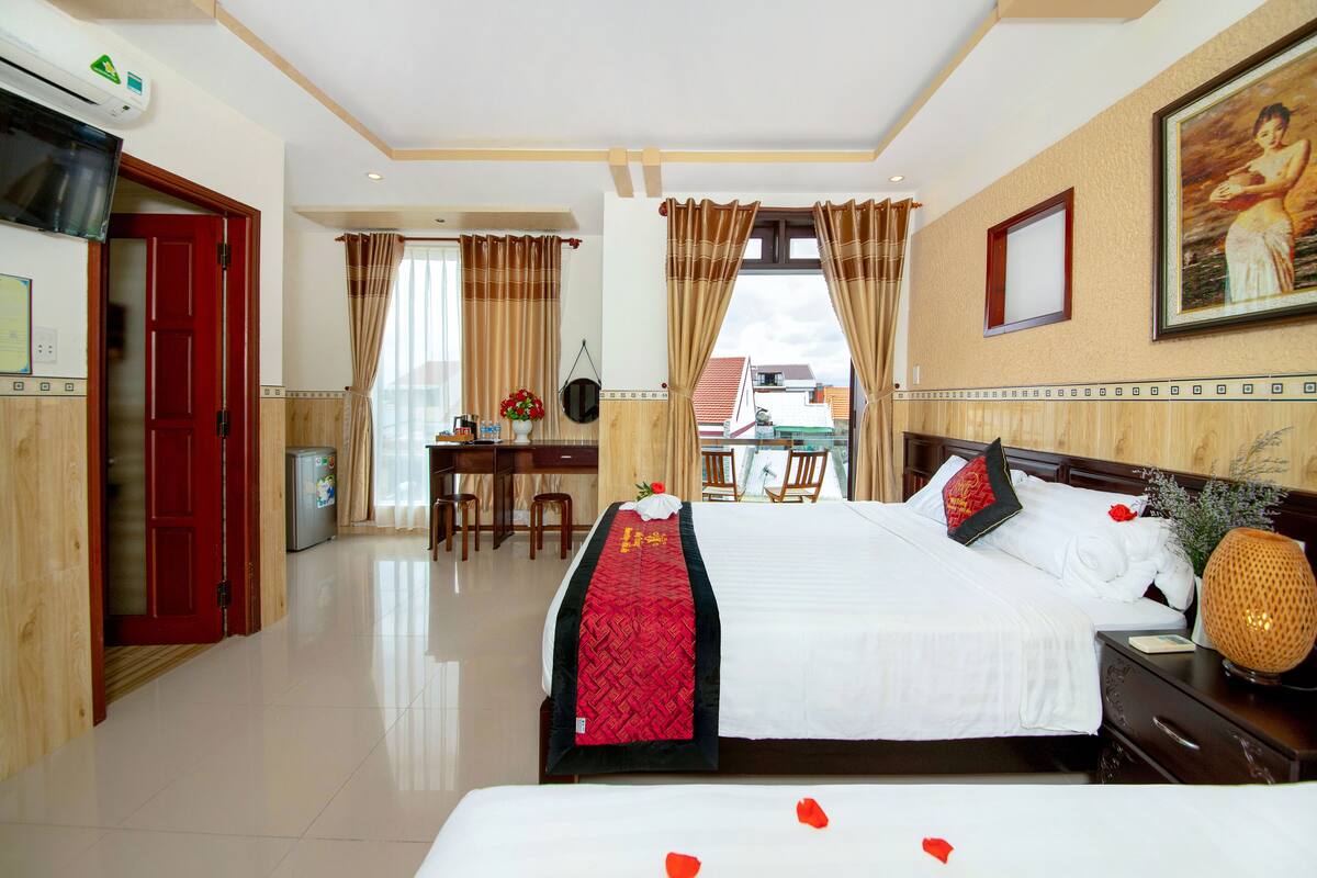 Habitación de hotel con cama, escritorio, silla, televisor y vistas al exterior.