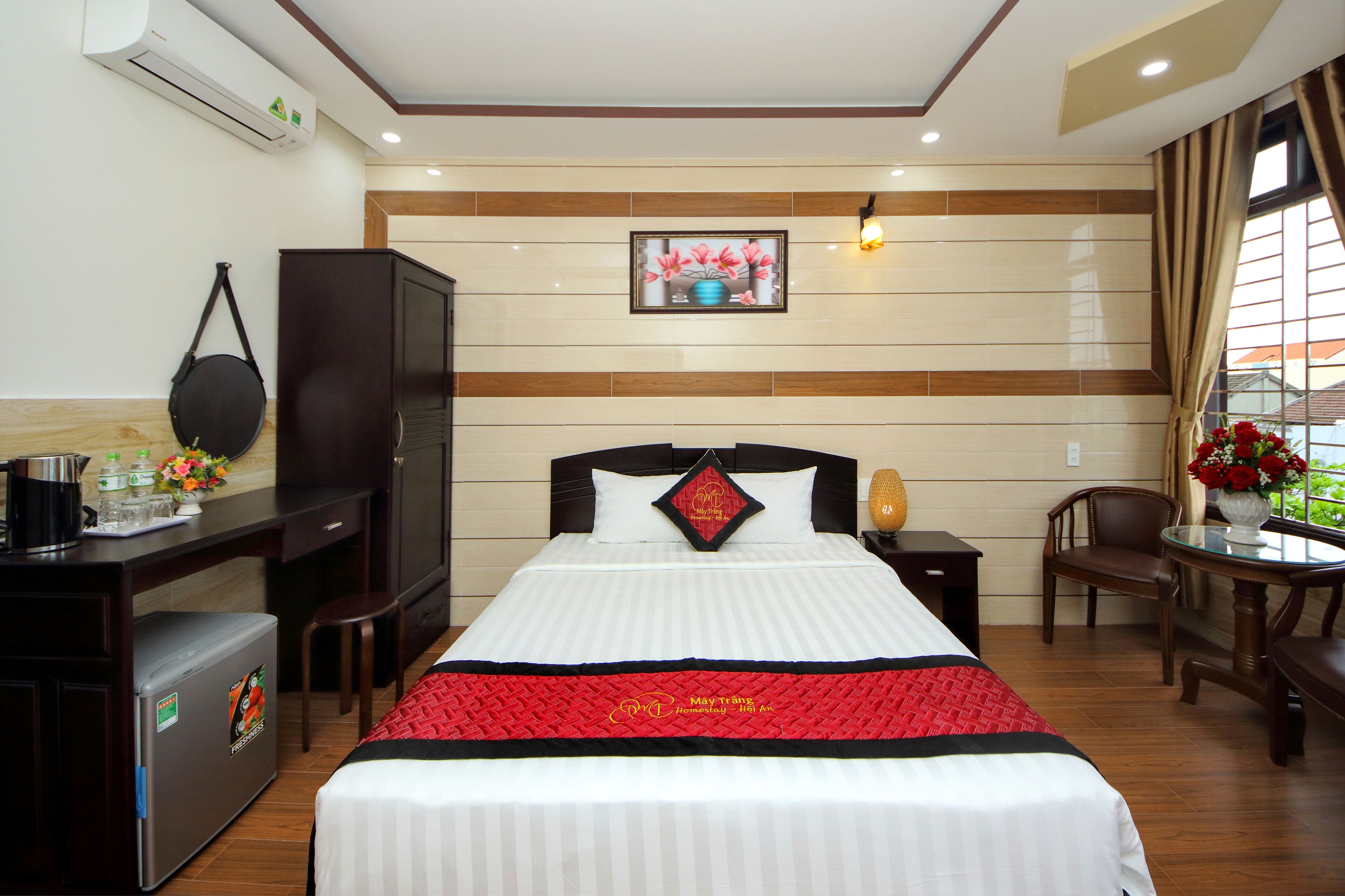 A hotel room with a bed, a desk, a refrigerator, a chair, and a window with curtains.